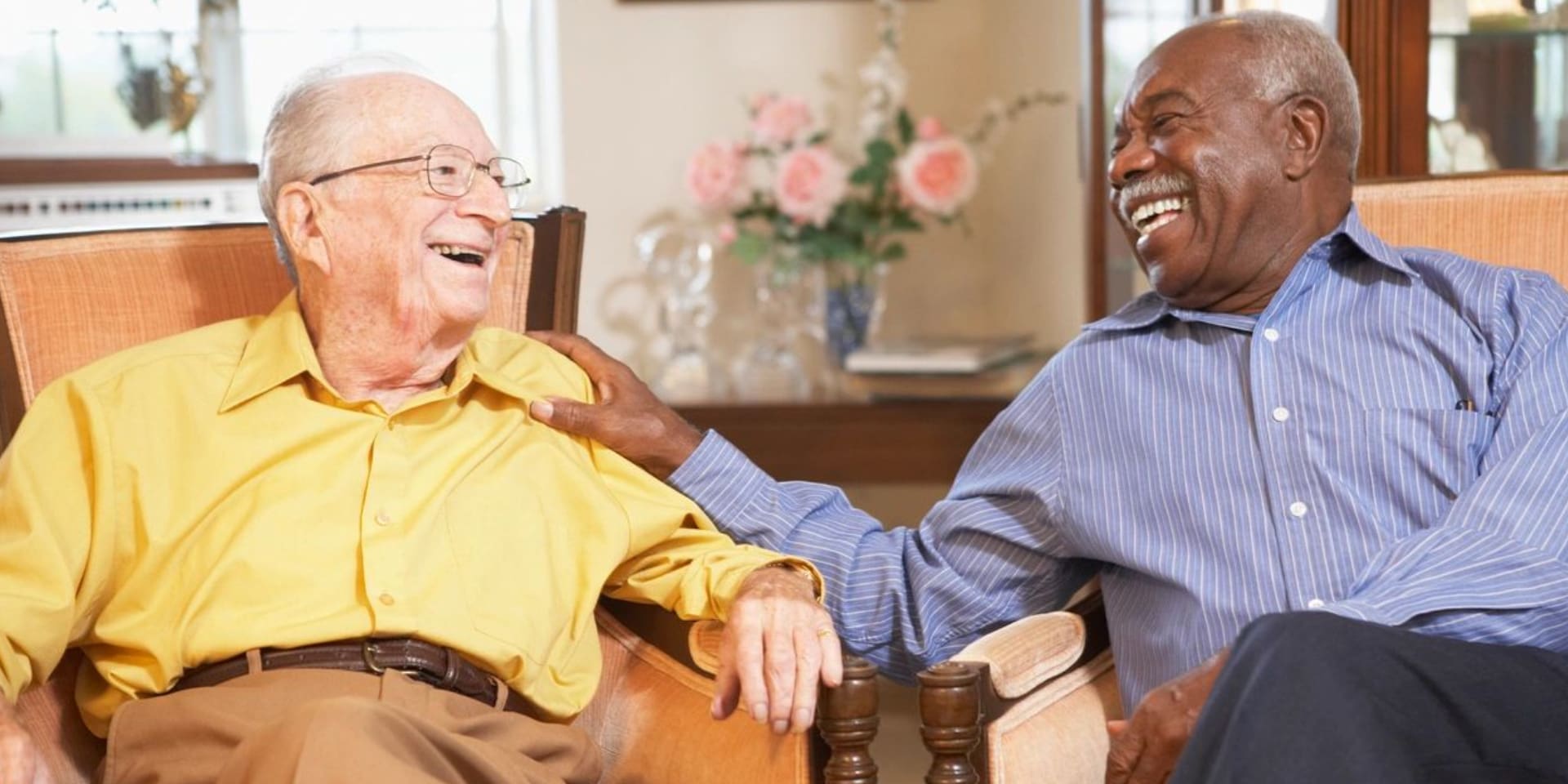 Two older men sitting in a chair laughing.