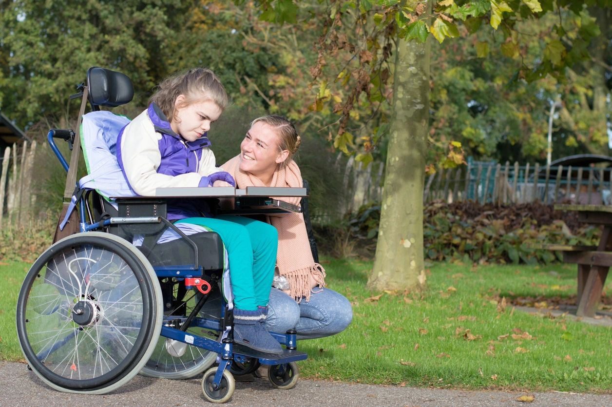 A man and girl sitting on the ground next to a wheelchair.