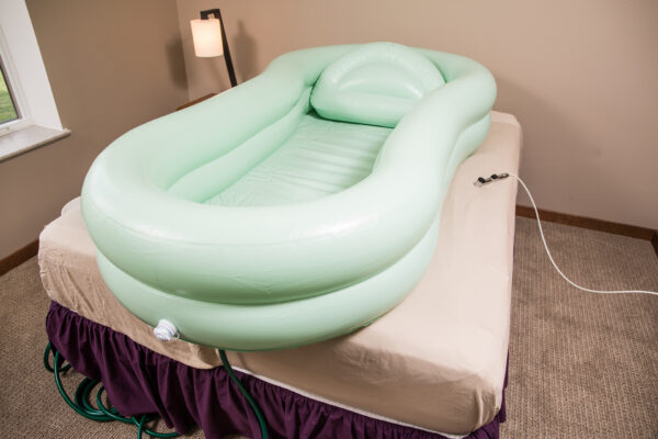 A green inflatable bathtub on top of a bed.